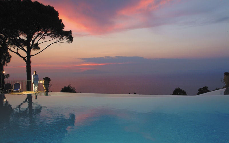 Luxury cliffside hotel in Capri with infinity pool overlooking Bay of Naples, Mediterranean palm trees and manicured gardens at sunset