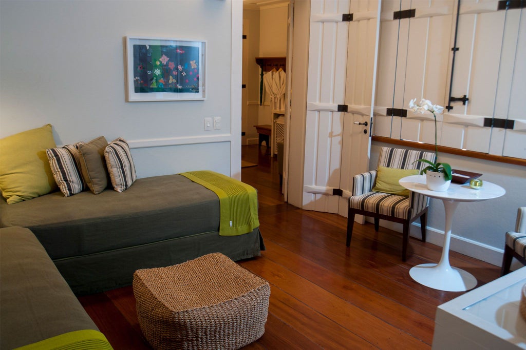 Elegant green-themed luxury suite with soft lighting, plush white bedding, and traditional Brazilian architectural details in a boutique hotel room