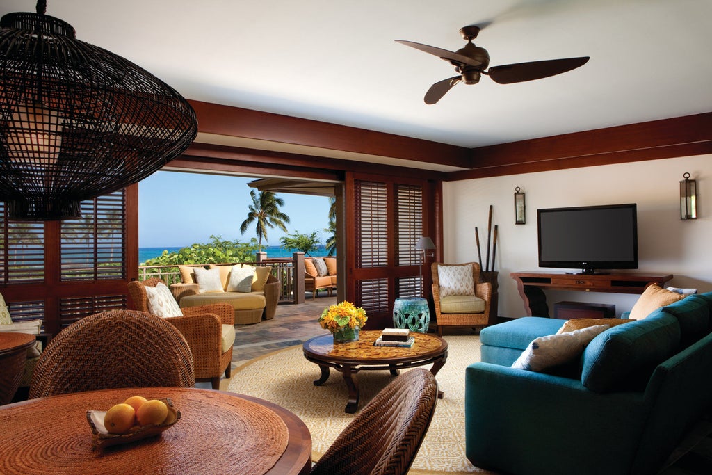 Infinity pool overlooking the Pacific Ocean with elegant lounge chairs, palm trees and lava rock features at luxury Hawaiian resort