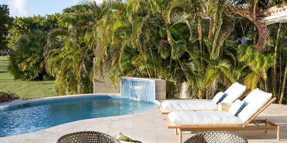 Luxurious pool suite with turquoise waters, white sun loungers, and elegant tropical decor overlooking pristine Antigua coastline at Jumby Bay resort