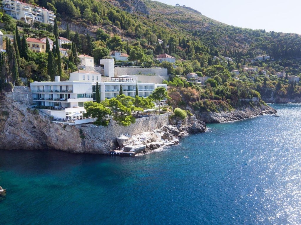 Modern luxury cliffside hotel with minimalist white facade overlooking the Adriatic Sea, surrounded by Mediterranean pine trees