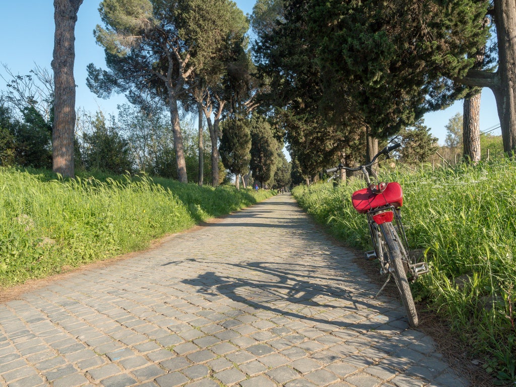 Ancient stone-paved Appian Way in Rome with vintage bicycles parked beside antique ruins, under towering cypress trees and blue sky