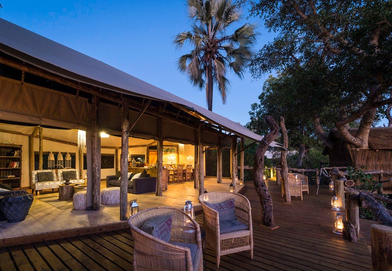 Elevated luxury safari tent with wooden deck overlooking lush African savanna, nestled among treetops at golden hour in Botswana