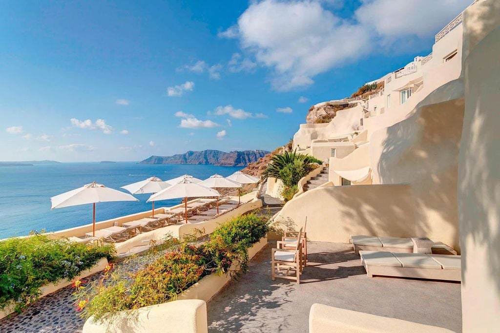 Beautiful white-washed luxury suites cascading down Santorini's cliffs, overlooking the deep blue Aegean Sea and volcanic caldera