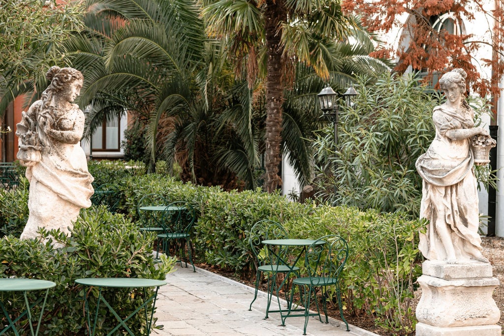 Elegant Italian palazzo hotel with soft terracotta facade, arched windows, and lush green potted plants against a warm afternoon light in Venice