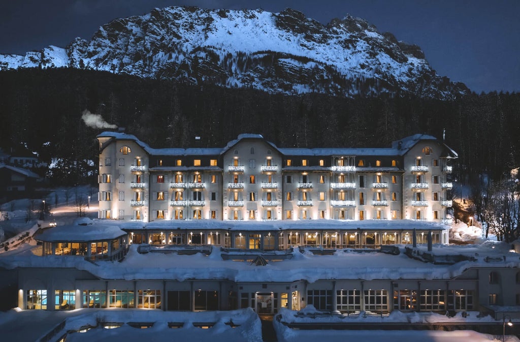 Elegant mountain resort with ornate white facade, grand balconies and snow-capped Dolomites backdrop, set amid manicured gardens