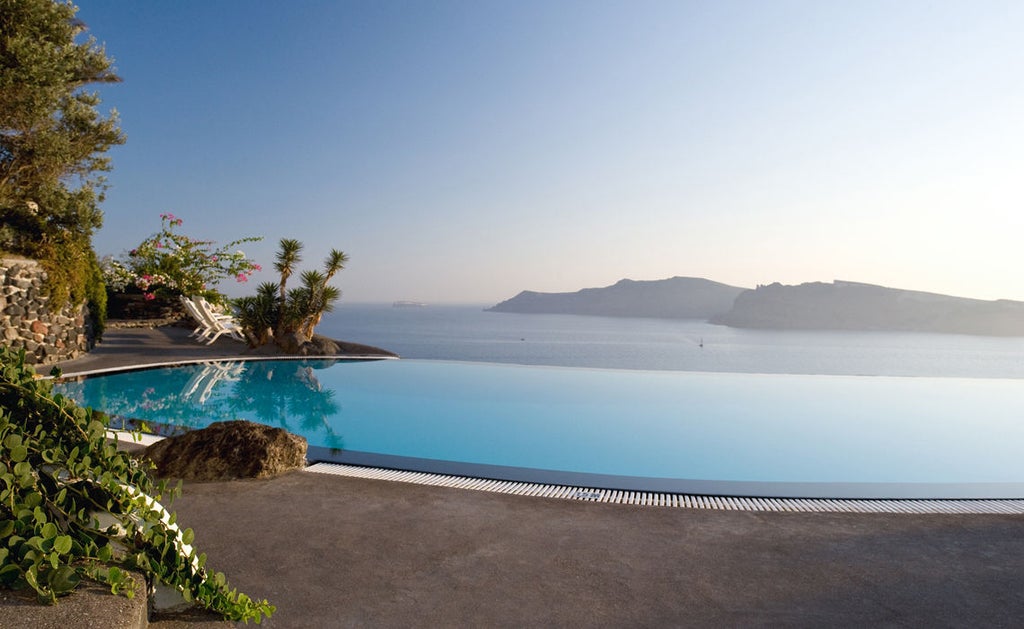 Whitewashed cave hotel built into Santorini cliffside with infinity pool overlooking Aegean Sea's deep blue waters at sunset