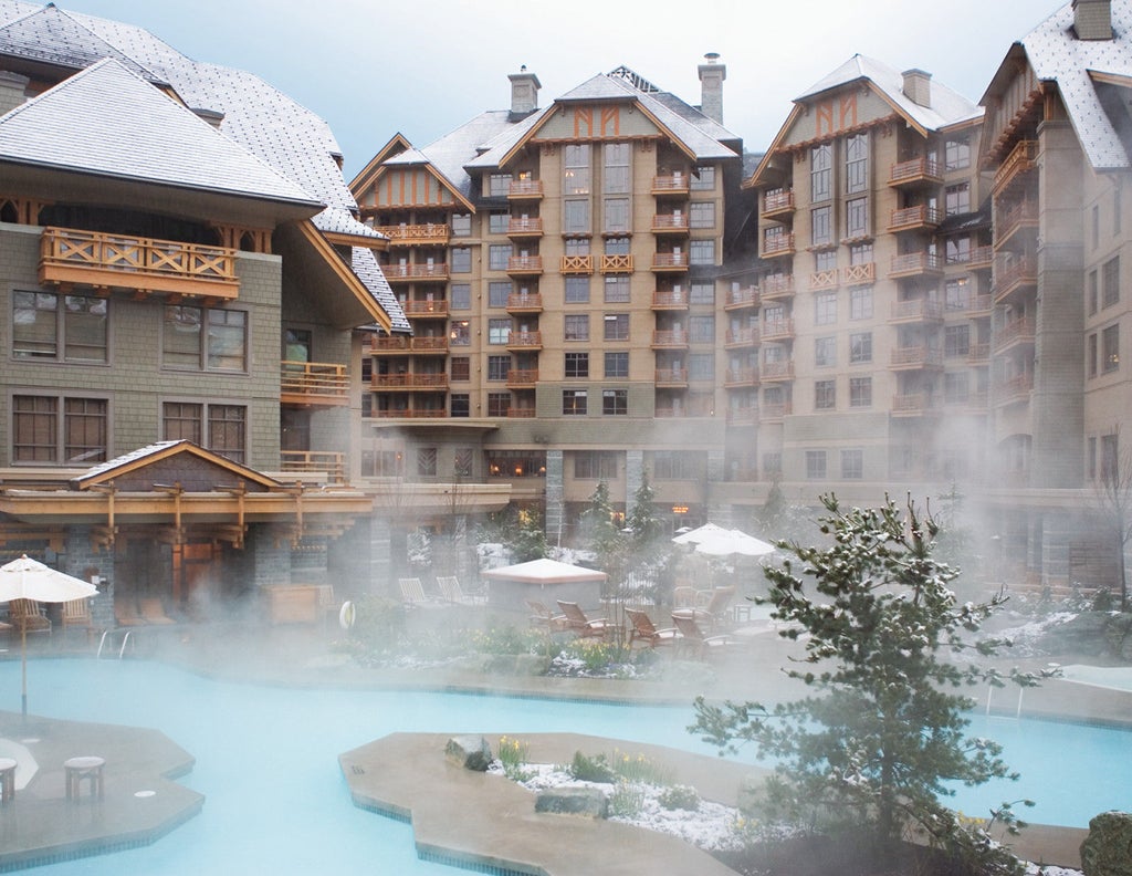 Majestic mountain-side luxury hotel with stone and timber facade, surrounded by snow-dusted pine trees and winter landscapes