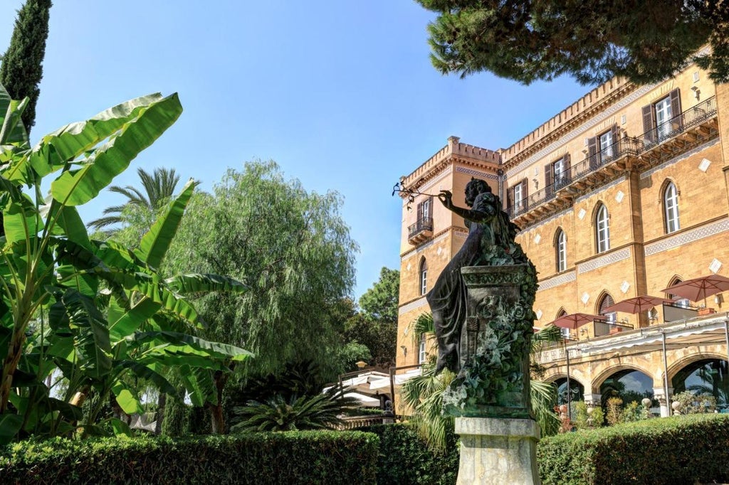 Elegant Mediterranean-style villa with ornate stone balconies and terraces overlooking Palermo Bay, surrounded by palm trees and manicured gardens