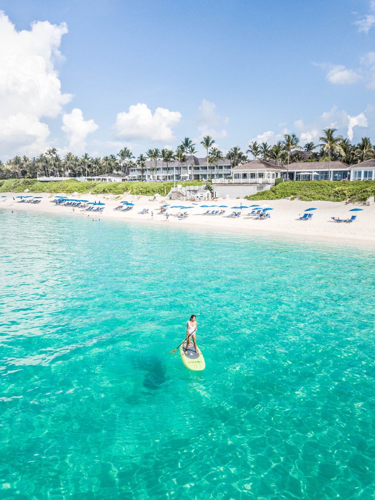 Elegant beachfront resort with white colonial-style buildings, swaying palm trees, and infinity pools overlooking turquoise Caribbean waters