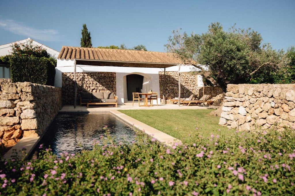 Luxurious whitewashed Spanish farmhouse hotel nestled in Menorca's countryside, with minimalist architecture and stone walls overlooking rolling landscape