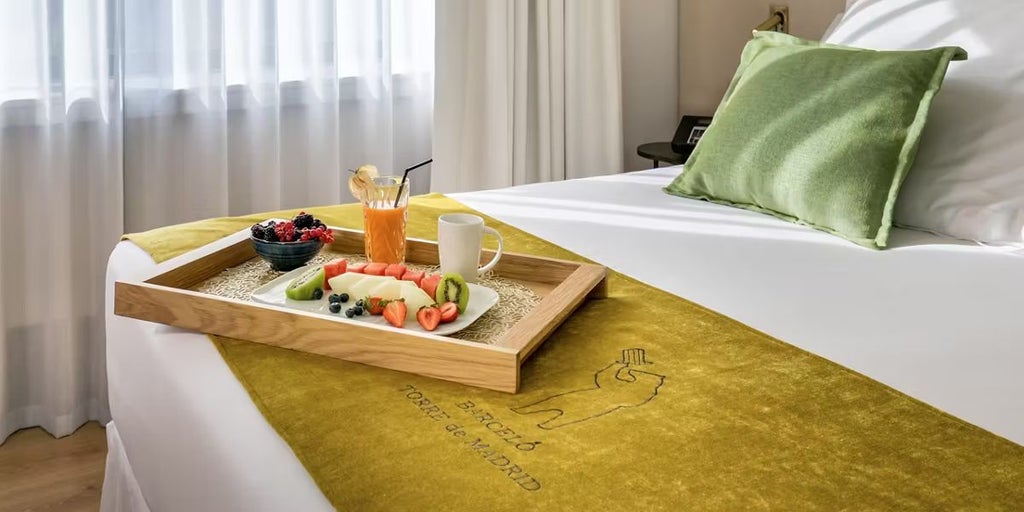 Elegant Deluxe hotel room with modern design, floor-to-ceiling windows overlooking Madrid skyline, plush king bed, and sleek contemporary furnishings