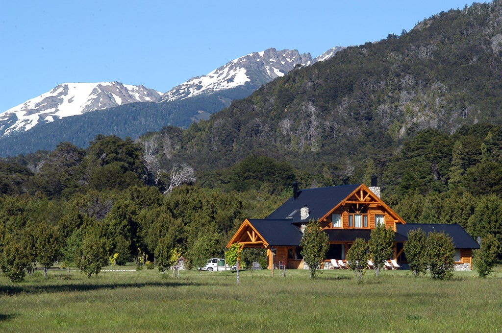 Luxurious mountain lodge nestled among snow-capped Patagonian peaks, with natural wood facade reflecting in pristine lake waters