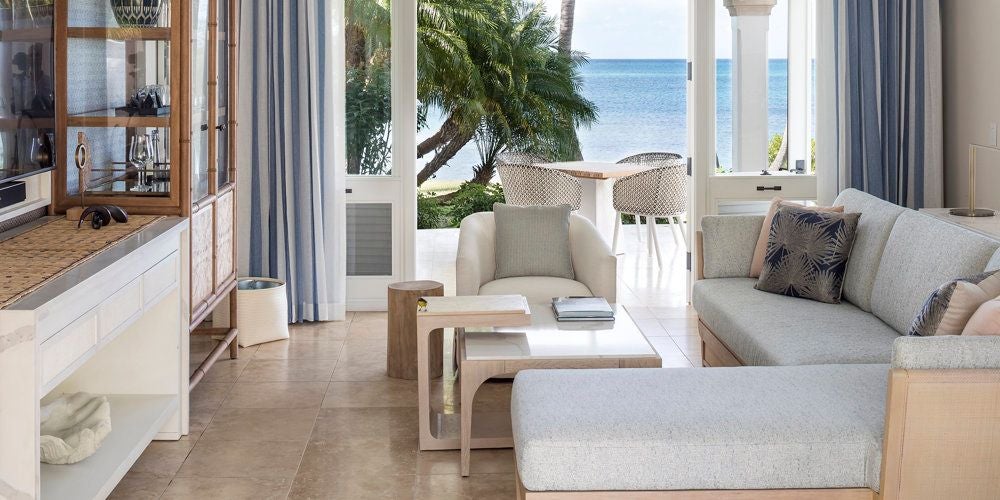 Luxurious beachside suite with white-draped four-poster bed, ocean view, and elegant tropical furnishings at Jumby Bay Island resort, Antigua