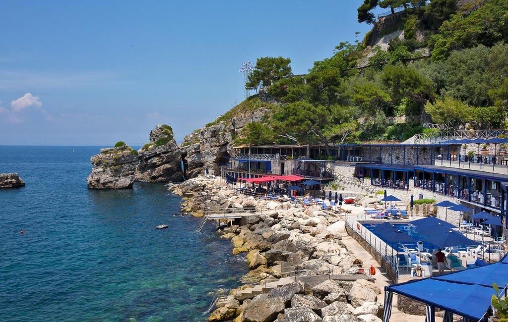 Elegant Italian coastal hotel with infinity pool overlooking the Gulf of Naples, nestled into rocky cliffside at sunset