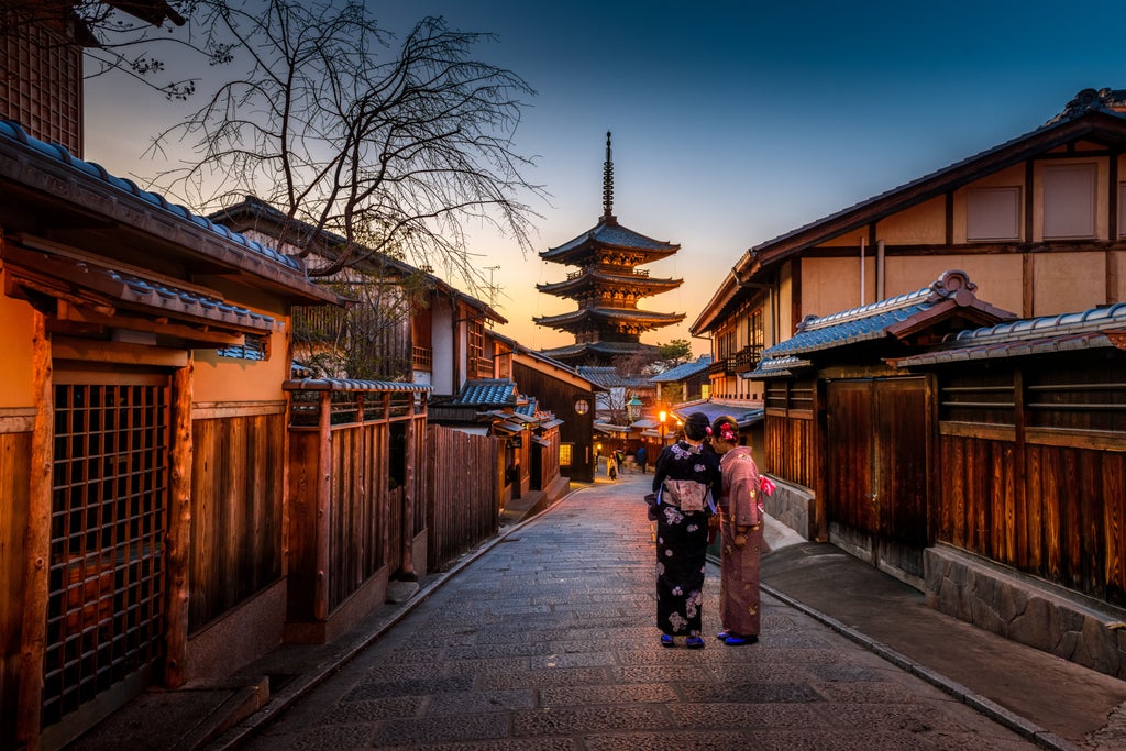 Traditional Japanese pagoda with red and gold accents rising above serene autumn maple trees at Kinkaku-ji Temple in Kyoto at sunset