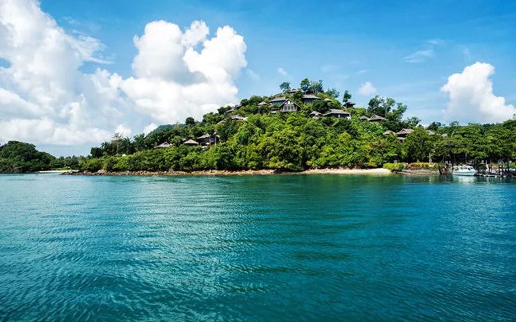 Luxurious infinity pool overlooking limestone cliffs and turquoise Phang Nga Bay waters, with cushioned lounge chairs at sunset