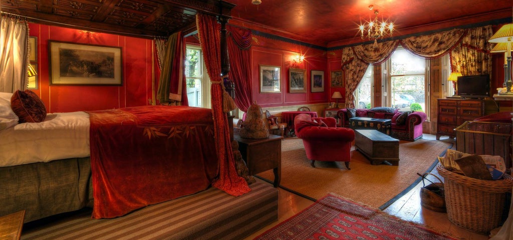 Elegant red-hued luxury suite with plush velvet headboard, ornate Victorian-style decor, and rich mahogany furnishings in a boutique UK hotel room