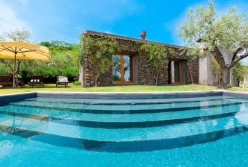 Elegant Sicilian deluxe room with rustic wooden floors, minimalist design, and expansive windows overlooking lush volcanic landscape at Monaci delle Terre Nere estate