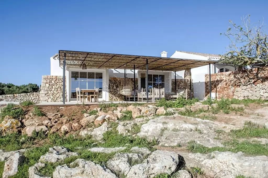 Historic stone tower hotel in Menorca with rustic limestone walls, elegant archways, and a manicured Mediterranean garden landscape