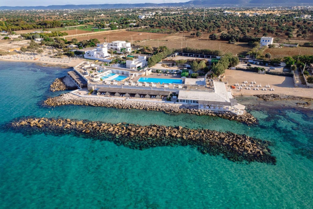 Luxurious coastal hotel with elegant infinity pool overlooking turquoise Mediterranean waters near scenic Italian shoreline at sunset