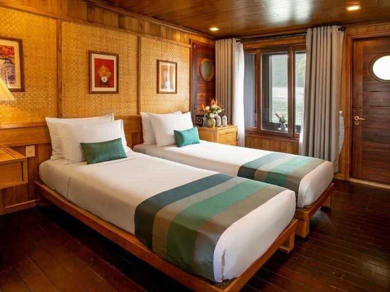 Elegant premium balcony cabin on Bhaya Cruises, featuring wood-paneled interior, plush bedding, and panoramic views of Halong Bay's emerald waters.