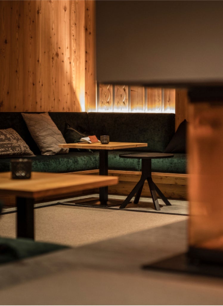 Traditional alpine lodge with modern glass and wood extension nestled in snowy Dolomites mountains at sunset, warm lights glowing within