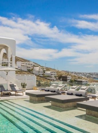 Luxurious white-washed hotel overlooking azure Aegean Sea, with elegant minimalist architecture and pristine infinity pool at sunset in Mykonos