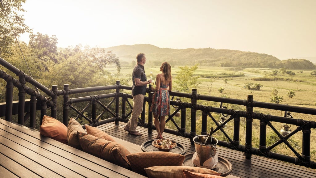 Luxury safari-style tent suite with private deck overlooking lush Thai jungle, featuring teakwood furnishings and outdoor daybed