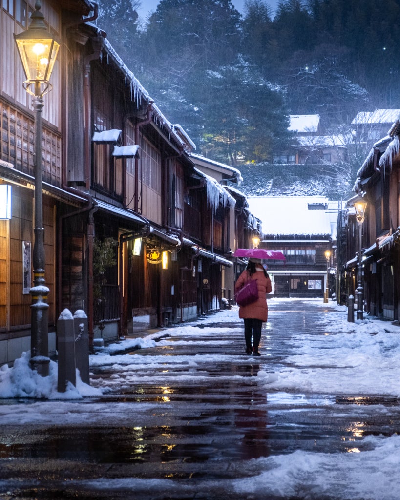 Elegant Japanese onsen entrance with lantern-lit stone path, wooden sliding doors and traditional bamboo garden under evening sky