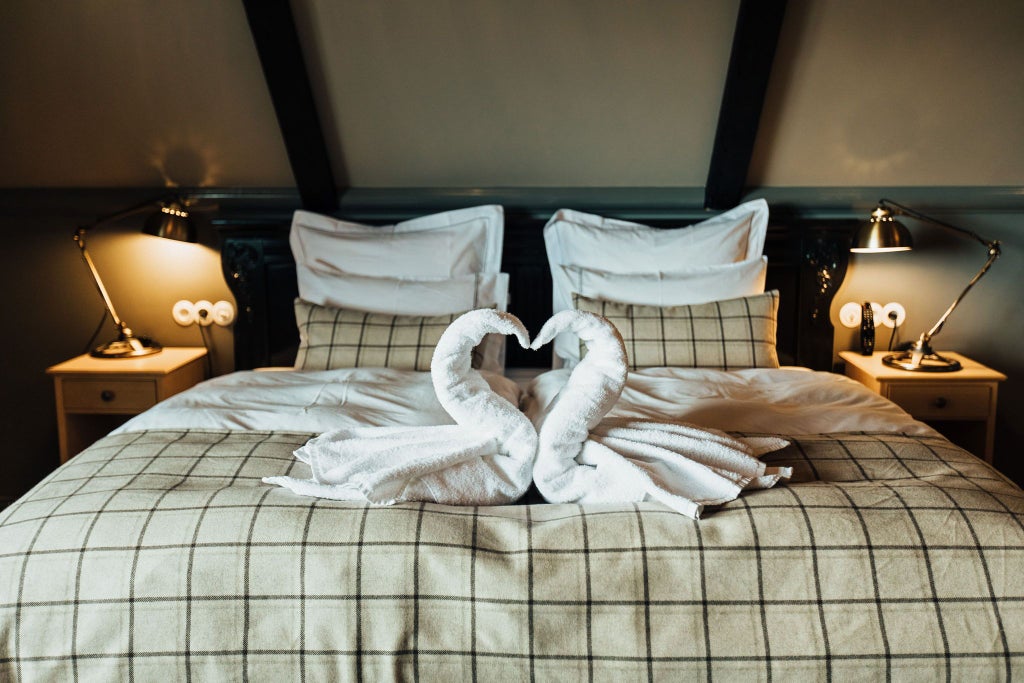 Elegant mini suite at Skálakot Manor Hotel, featuring plush white bedding, rustic wooden furniture, and panoramic Icelandic mountain views through large windows.