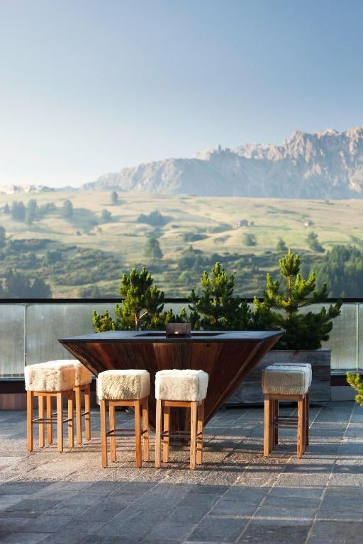 Modern luxury mountain hotel with glass facade nestled in snow-covered Dolomites peaks, featuring panoramic terraces and outdoor pool