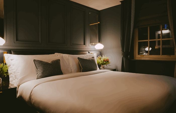 Elegant boutique hotel room with plush emerald-green velvet headboard, soft ambient lighting, and sophisticated contemporary design in a luxe London setting