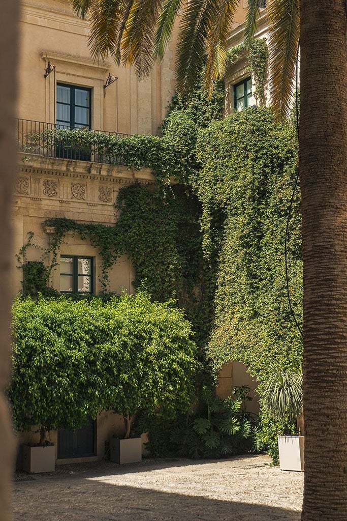 Elegant Sicilian villa with terracotta-tiled roof, stone walls, lush garden, and panoramic view of Noto's historic landscape at golden hour