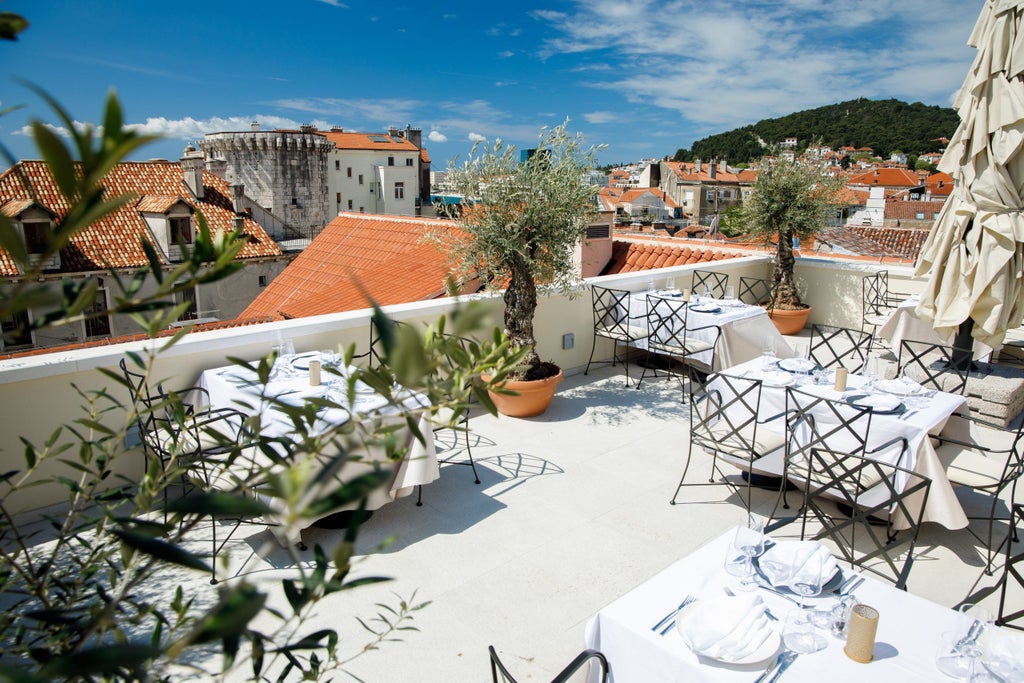 Elegant beachfront hotel with white stone facade, private balconies and red-tiled roof overlooking the crystal blue Adriatic Sea at sunset