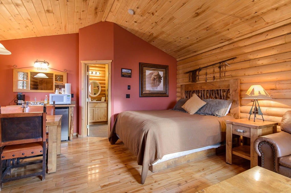 Rustic wooden cabin suite interior with plush king bed, warm earth tones, large windows overlooking scenic mountain landscape at scenic ranch property