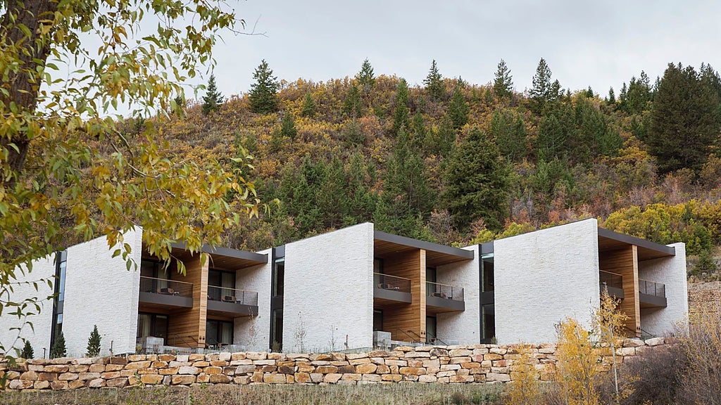 Contemporary luxury mountain lodge with stone walls and floor-to-ceiling windows, nestled in snowy Utah wilderness under clear blue skies