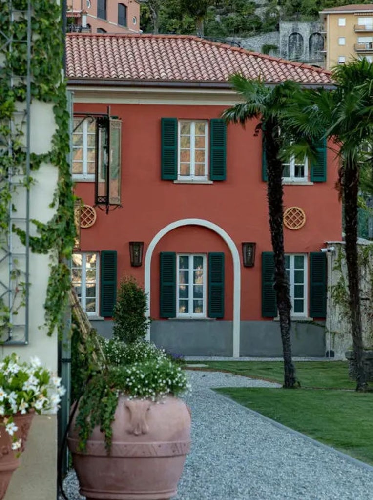 Elegant hotel facade with stone balconies and arched windows overlooks Lake Como, surrounded by manicured gardens and cypress trees