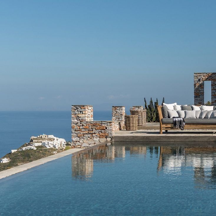 Luxurious white Cycladic-style hotel with minimalist design overlooking azure Aegean Sea, featuring clean lines and panoramic infinity pool at sunset