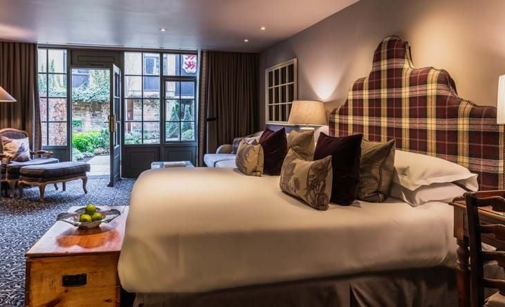 Luxurious open-plan suite with elegant furnishings, soft neutral tones, and a large window overlooking a charming courtyard at The Lygon Arms.