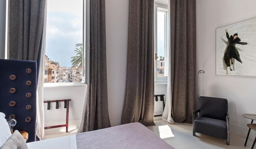 Elegant Roman studio with soft neutral decor, large windows overlooking historic scenset near Spanish Steps, featuring plush white bedding and minimalist contemporary furnishings