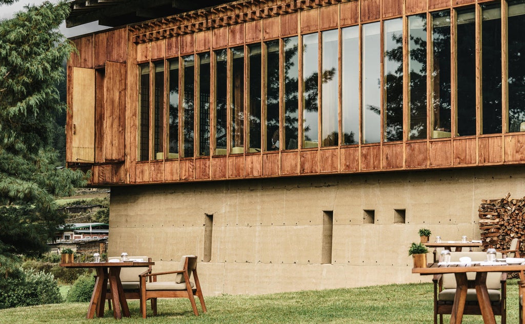 Luxury mountain lodge with floor-to-ceiling windows overlooking misty Bhutanese valley, traditional architecture meets modern design