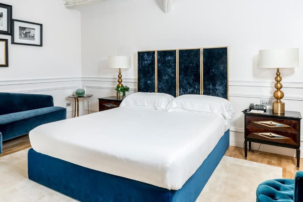 Elegant Italian junior suite with plush white bedding, marble accents, floor-to-ceiling windows overlooking scenic landscape at Palazzo Dama hotel