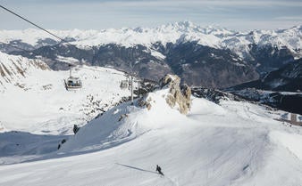 Snow-covered luxury alpine hotel with wooden balconies nestled among pine trees, featuring sloped roofs and mountain backdrop in Courchevel