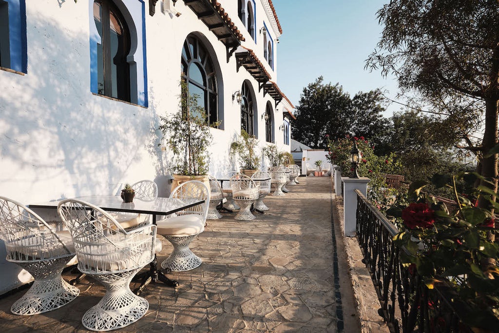 Traditional Moroccan riad with ornate archways, vibrant blue pool in courtyard surrounded by lush plants and luxurious lounge seating