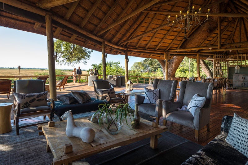 Elevated luxury safari lodge with thatched roof suites on wooden stilts overlooking vast Okavango Delta grasslands at sunset