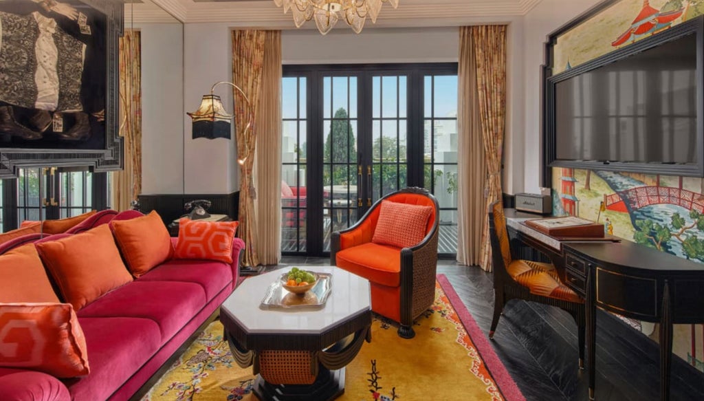 Opulent hotel suite with vintage opera-inspired decor, featuring a velvet chaise lounge, crystal chandelier and gold-framed art on emerald walls