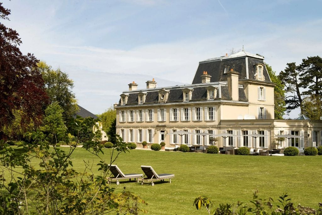 Grand 18th-century French château hotel with elegant cream facade, manicured gardens, and classic architecture set amid lush countryside