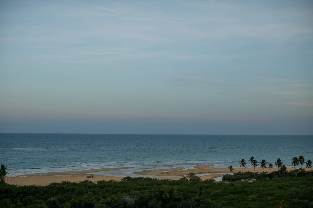 Luxurious Brazilian beachfront pousada with white-washed architecture, lush tropical gardens, and elegant outdoor seating nestled in Trancoso's scenic coastal landscape