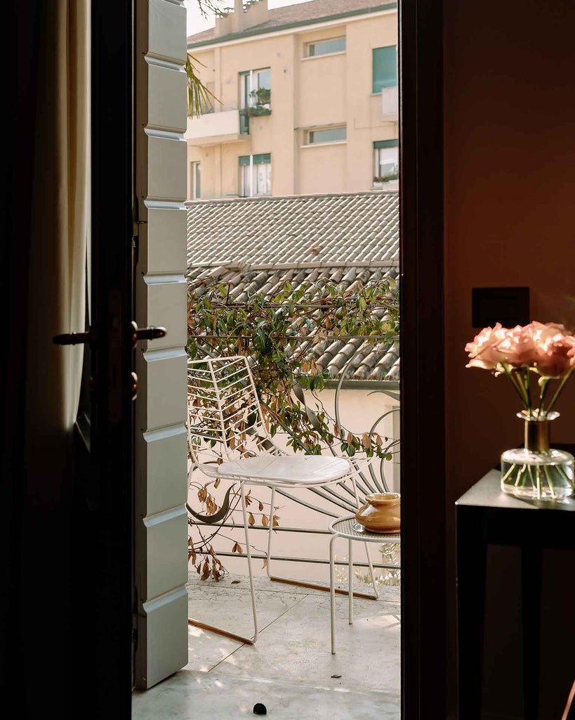 Elegant Italian suite with plush king bed, soft cream linens, ornate gold-framed artwork, and large arched window overlooking scenic countryside landscape